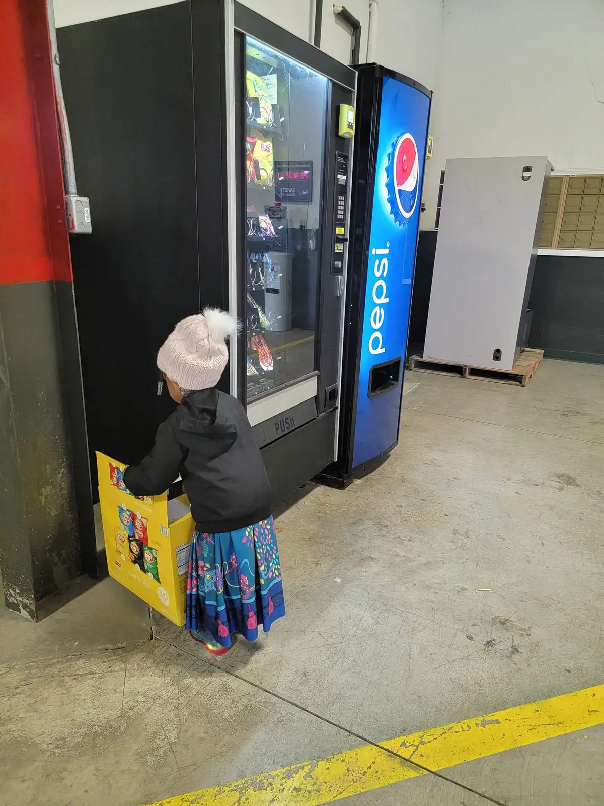 Ryleigh carrying a box of snacks beside vending machines